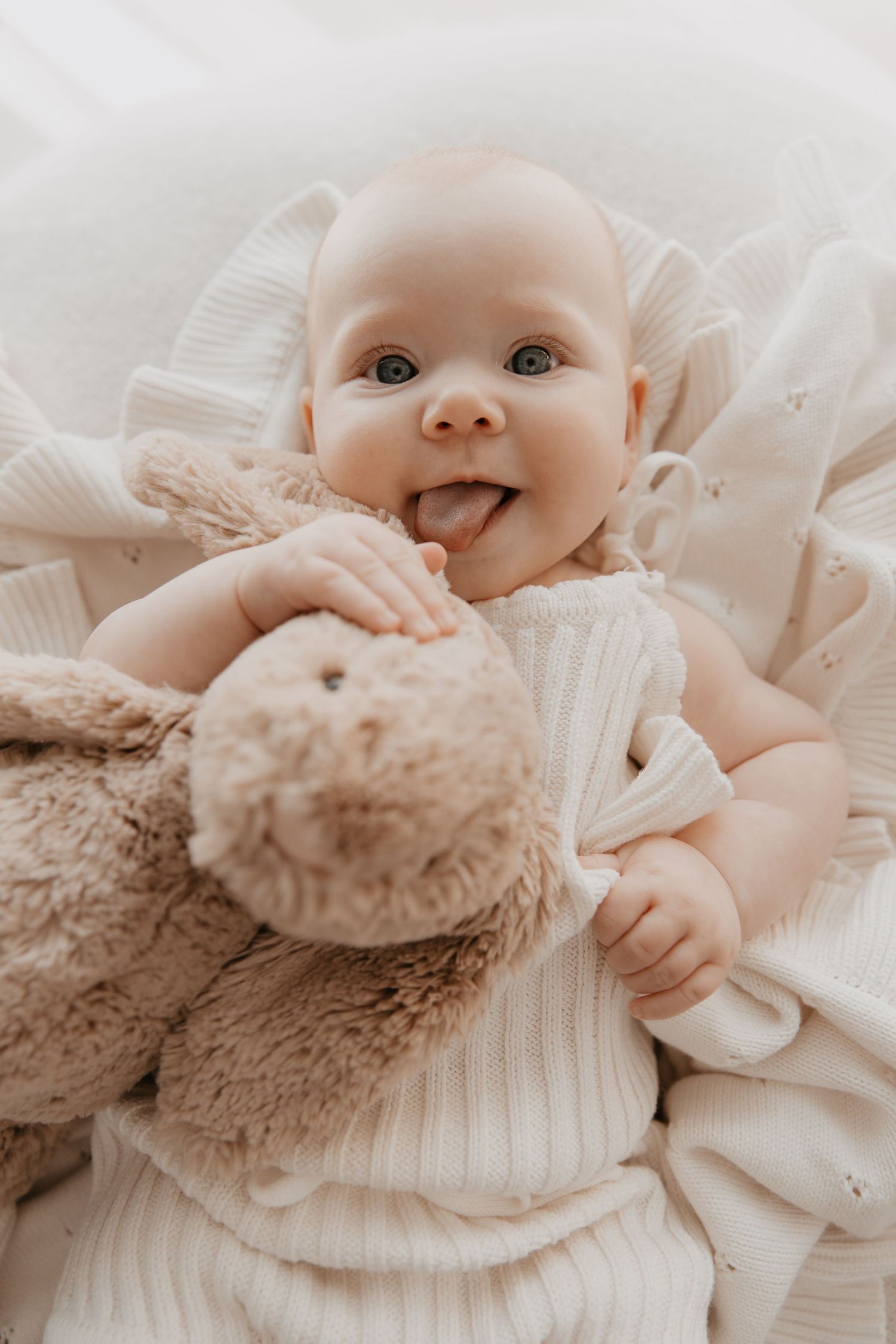 3 month old baby girl poking tongue out & cuddling bunny in a newborn studio session with Gray + Bear Photography in Ipswich