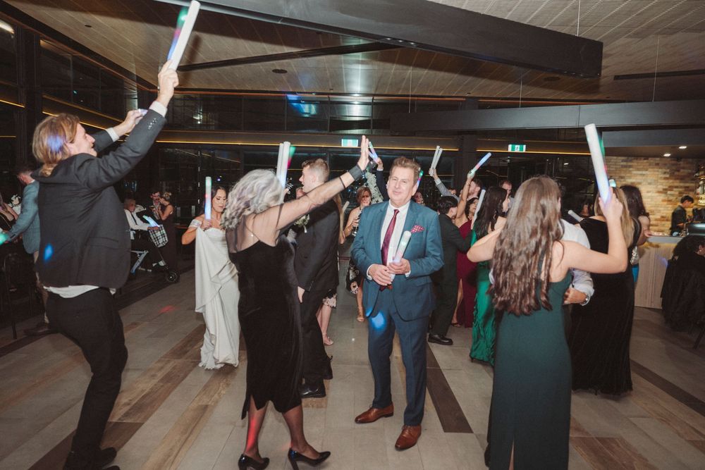 Guests dancing and waving glow sticks at a formal wedding reception on a dance floor.