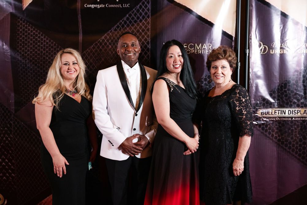 Several people pose and smile together in elegant formal attire at a glamorous evening event.