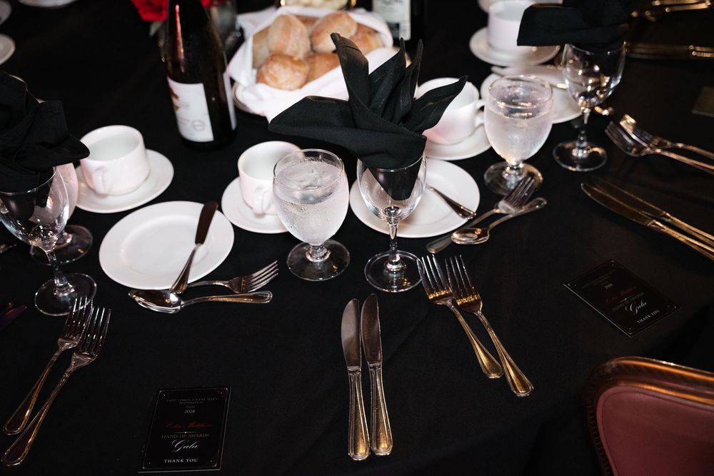 White coffee cups and saucers with golden silverware arranged on a dark table at an elegant dining setting.
