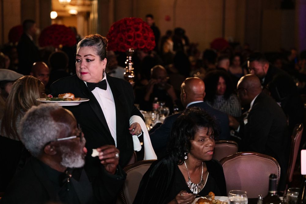 Guests seated at formal dinner tables during an elegant evening gala event with dark lighting and formal attire.