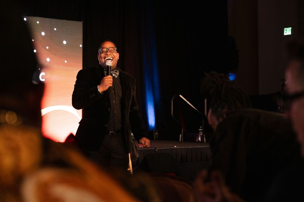 A performer sings on stage at a dimly lit venue with warm lighting and string lights in the background.