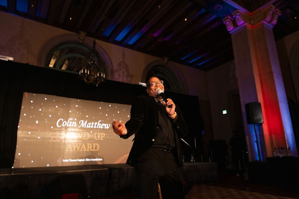 Event venue illuminated with blue ambient lighting and projection screens showing text displays.