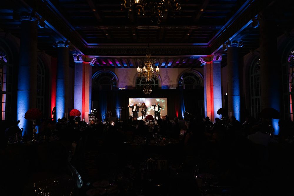 Large event venue with dramatic red and blue lighting illuminating pillars and a central projection screen in a darkened room.