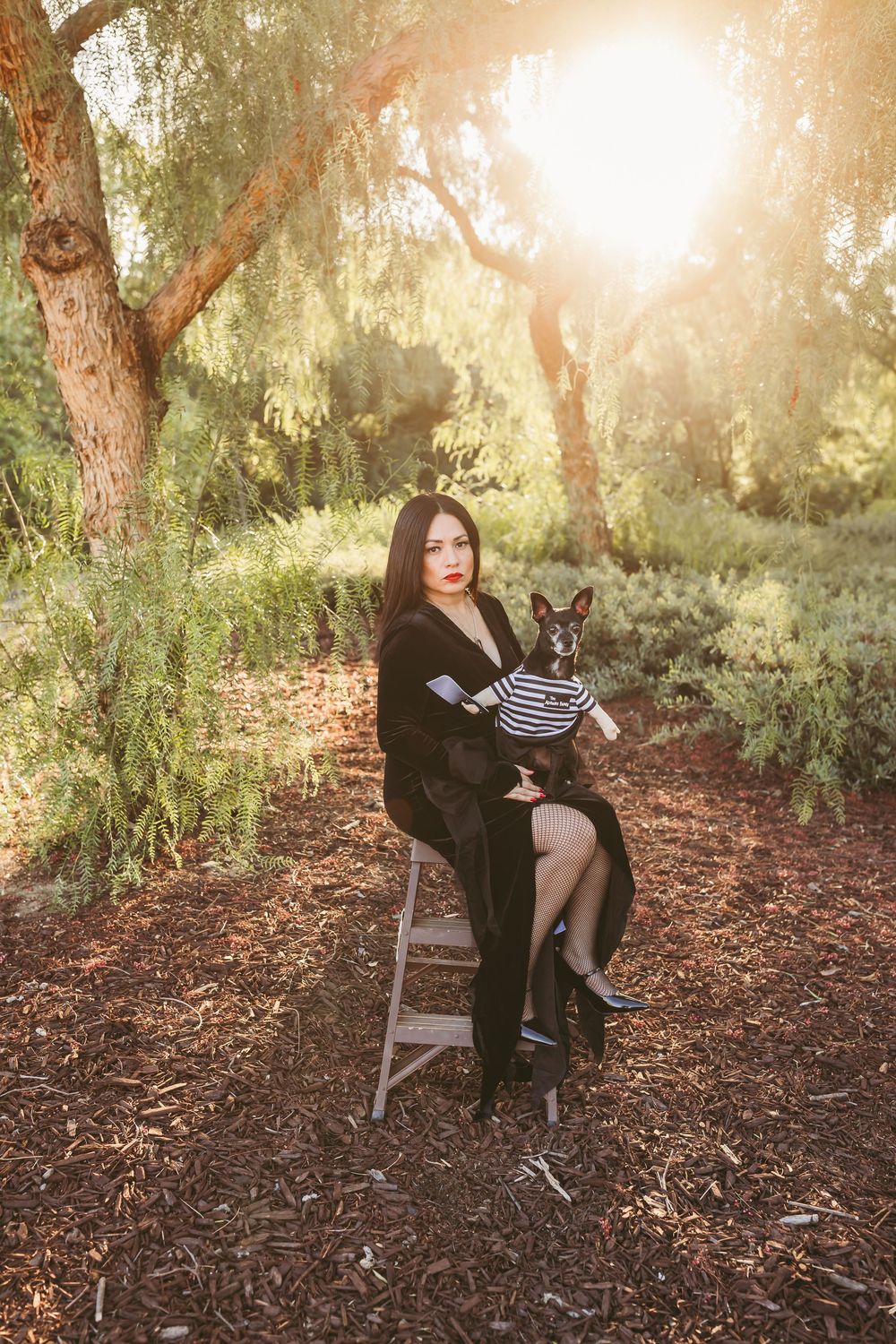 A charming outdoor portrait session in a sunlit wooded area with a rustic wooden chair as the focal point.