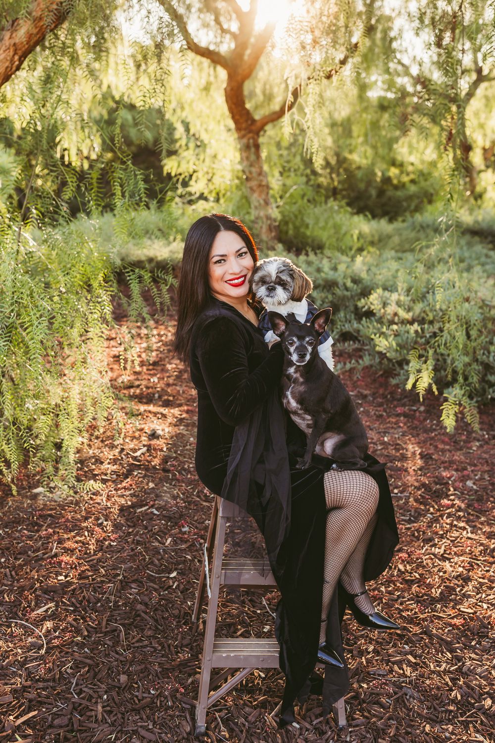 A person in black clothing sits on a rustic wooden bench with their small gray and white dog in an autumn garden setting.