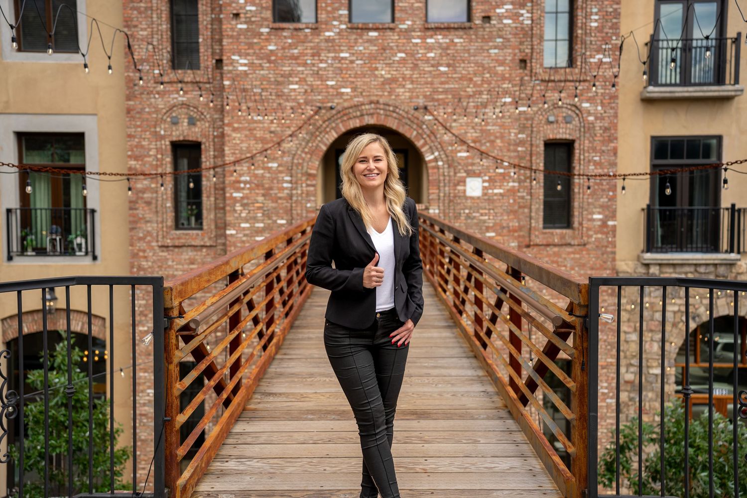 Two people walk across a wooden footbridge connecting brick buildings in an urban courtyard setting.