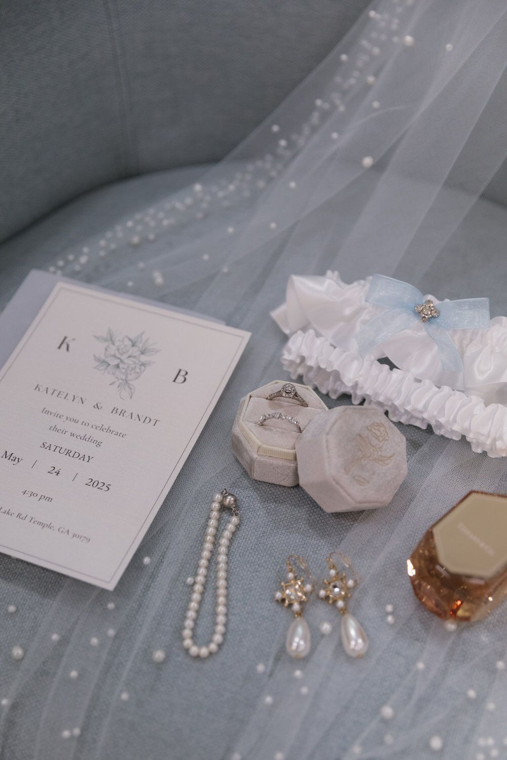 wedding detail flat lay of rings, a pearl necklace, the wedding invitation, earrings, perfume and garter