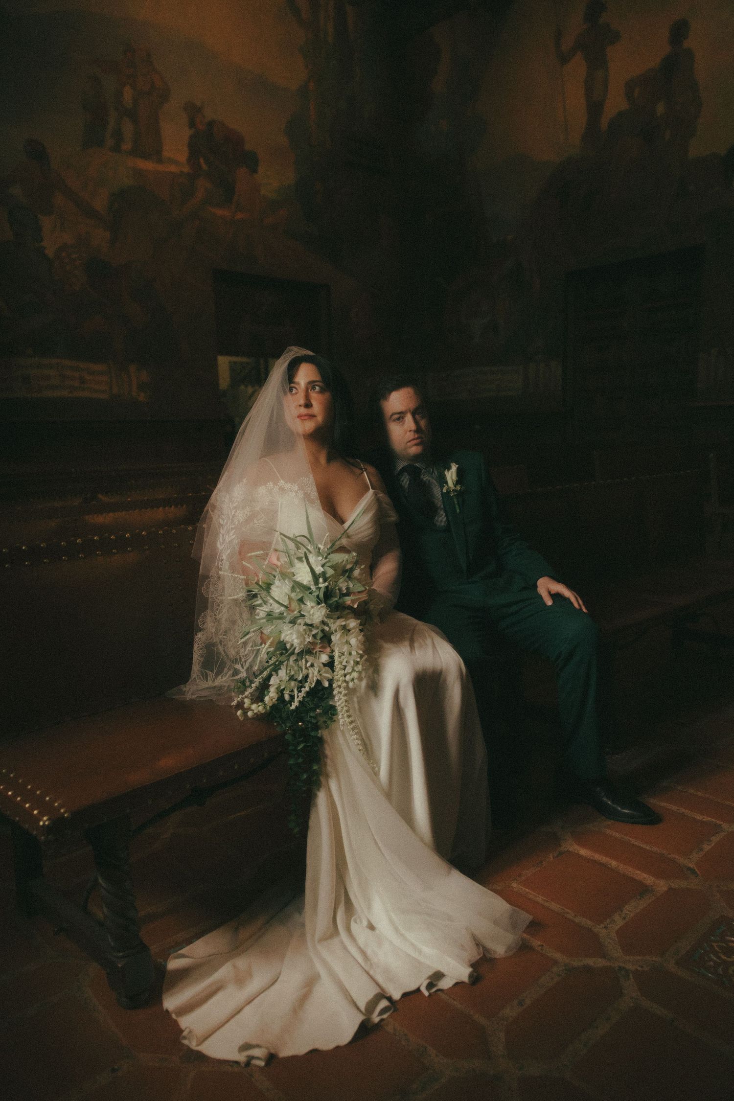 Romantic wedding couple embraces in intimate candlelit church setting with moody lighting and flowing veil.