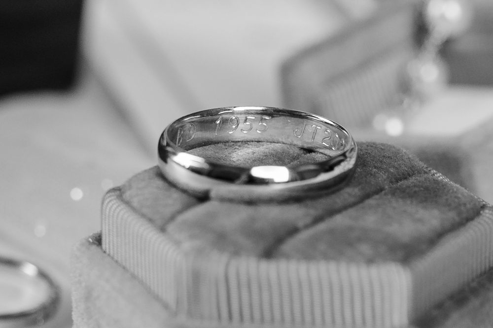 Close up macro shot of a silver wedding ring with a sparkly diamond resting on a textured surface in black and white.