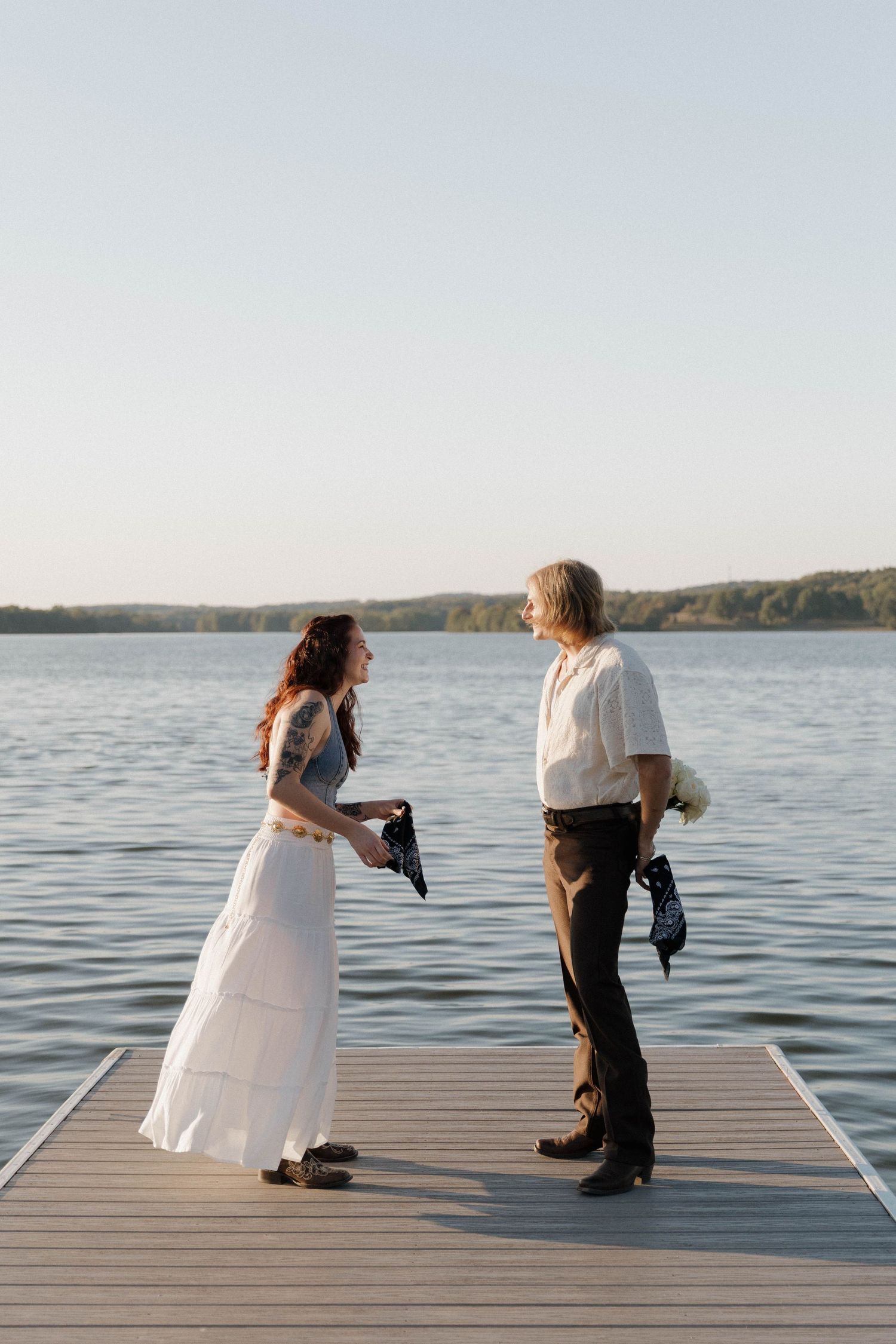 Two photographers with cameras capture sunset photos from a wooden dock overlooking a serene lake.