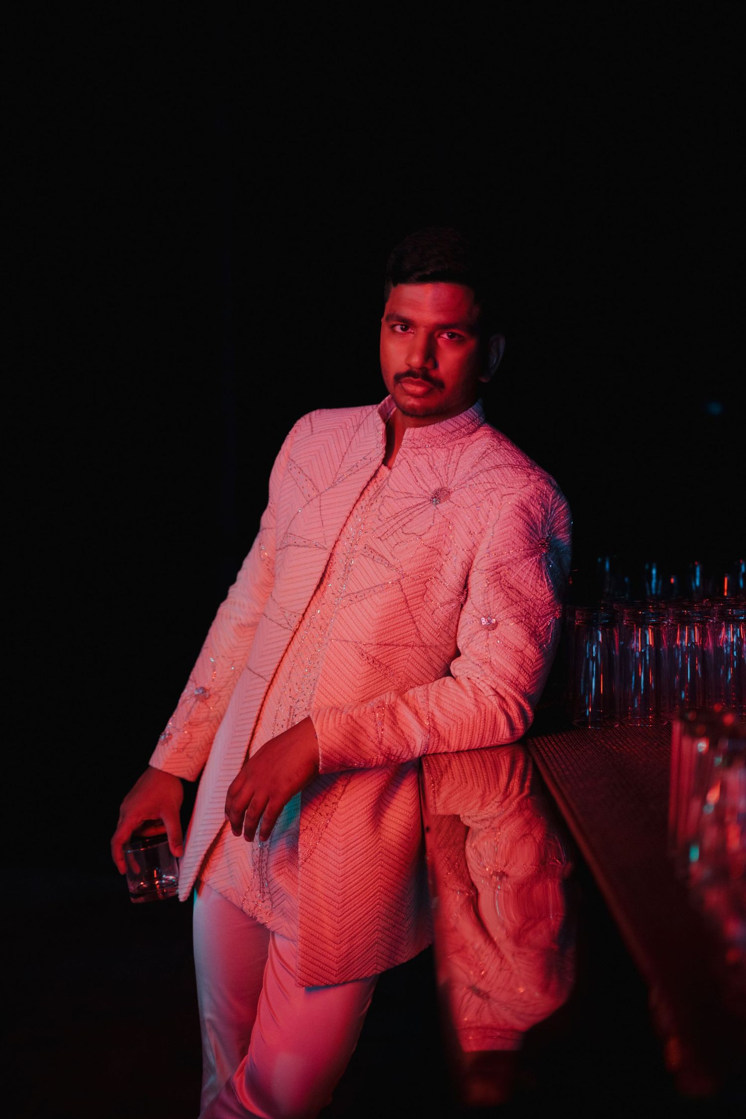 Person in white jacket illuminated by red lighting in dark nightclub setting.