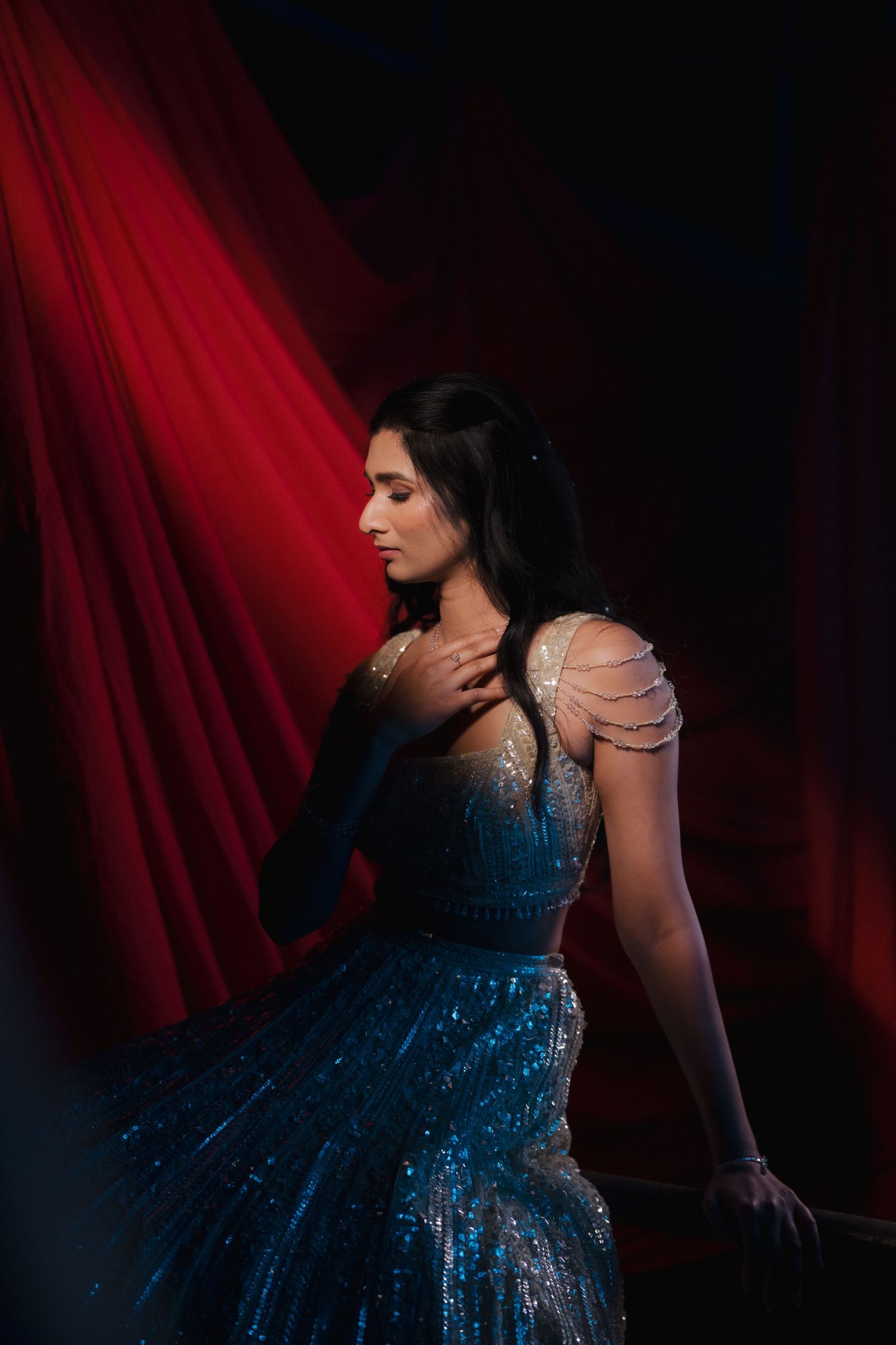 A person in a sparkling navy blue evening gown poses dramatically against a deep red curtain backdrop.