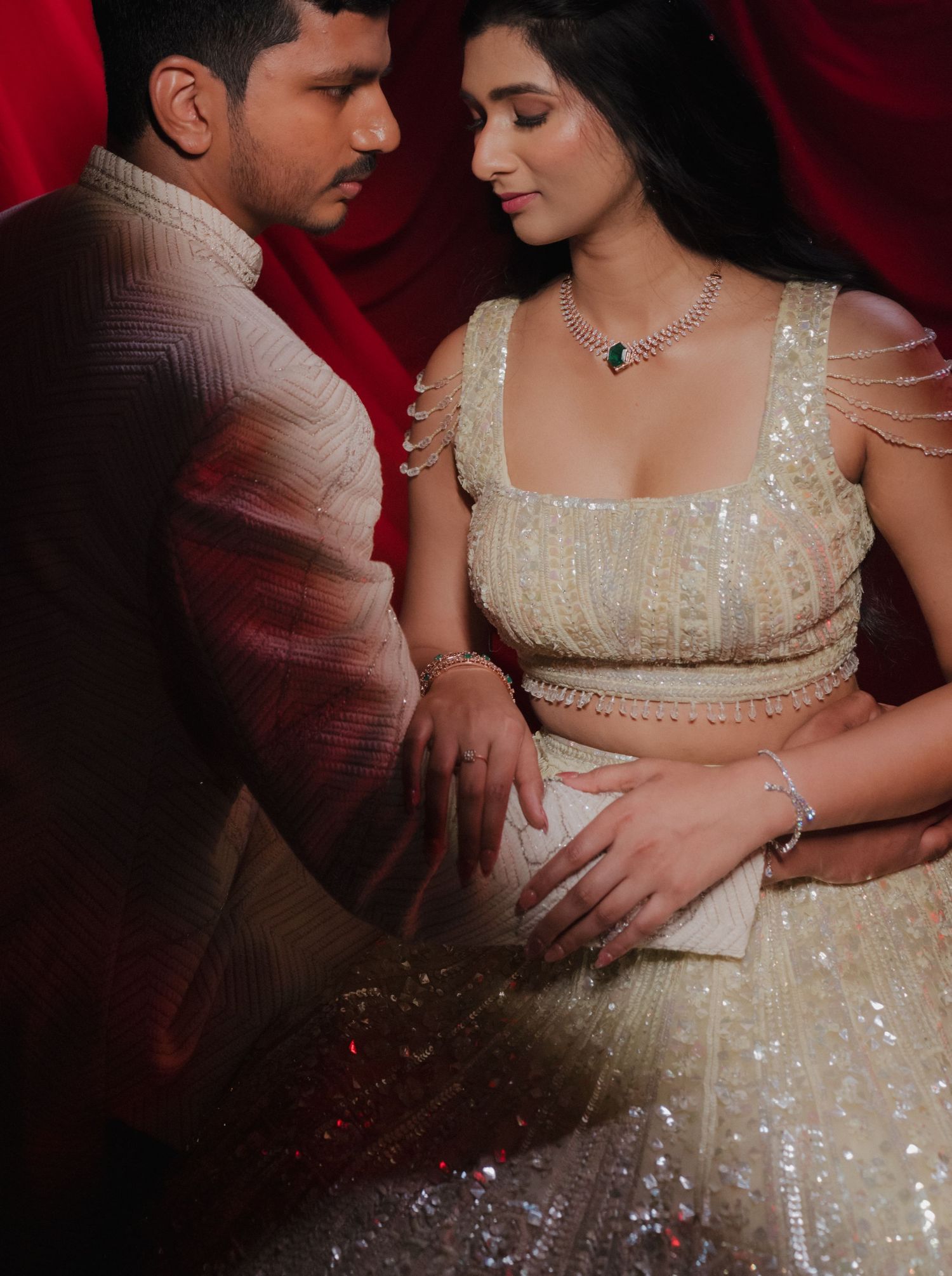 Close-up of a couple dressed in evening attire embracing against a deep red background.