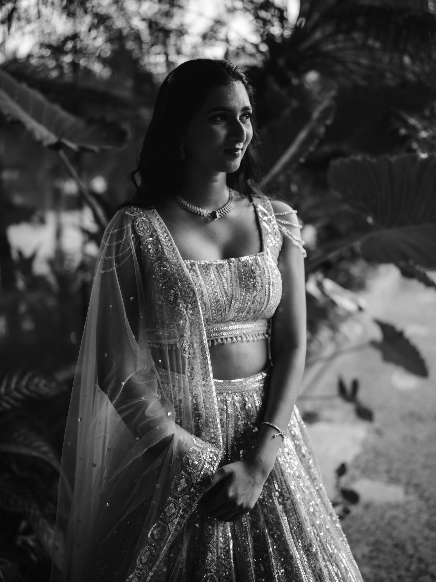 Artistic black and white portrait showing intricate details of an embroidered lehenga dress in natural lighting.