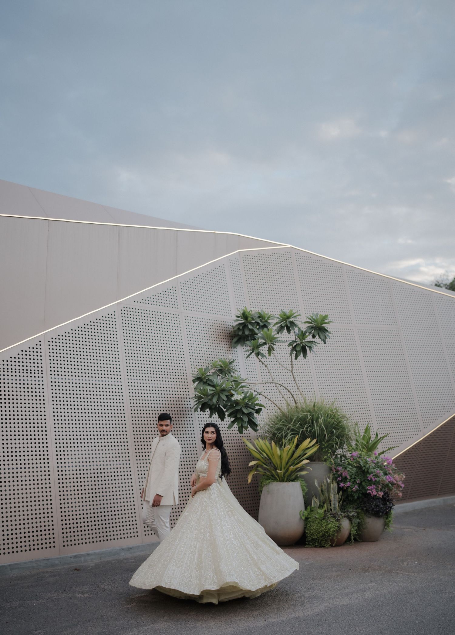 A couple poses for wedding photos against a modern white geometric wall with tropical plants and palm trees.
