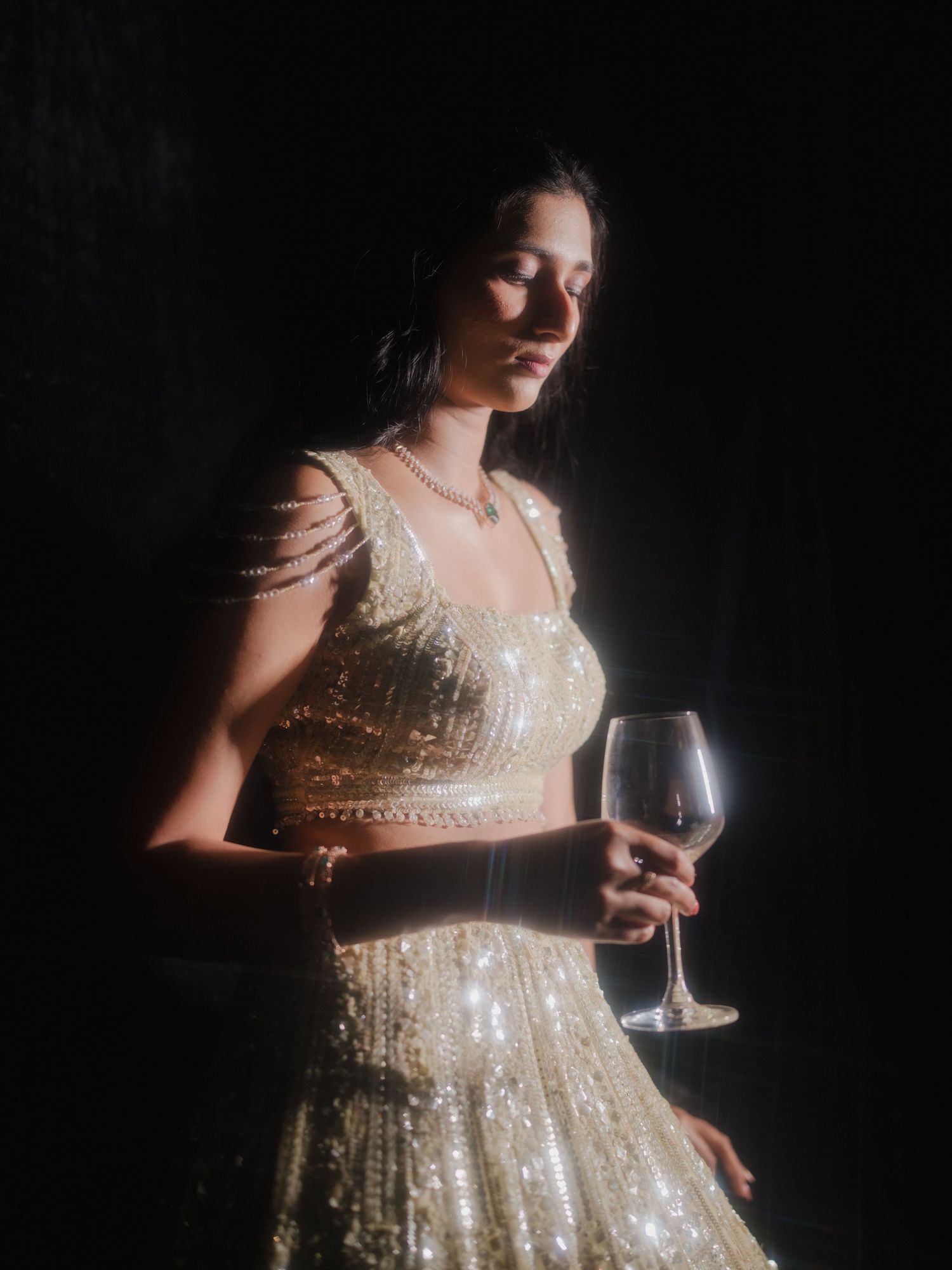 A woman in a sparkly beige gown holds a wine glass against a dark background in a dramatic moody portrait series.