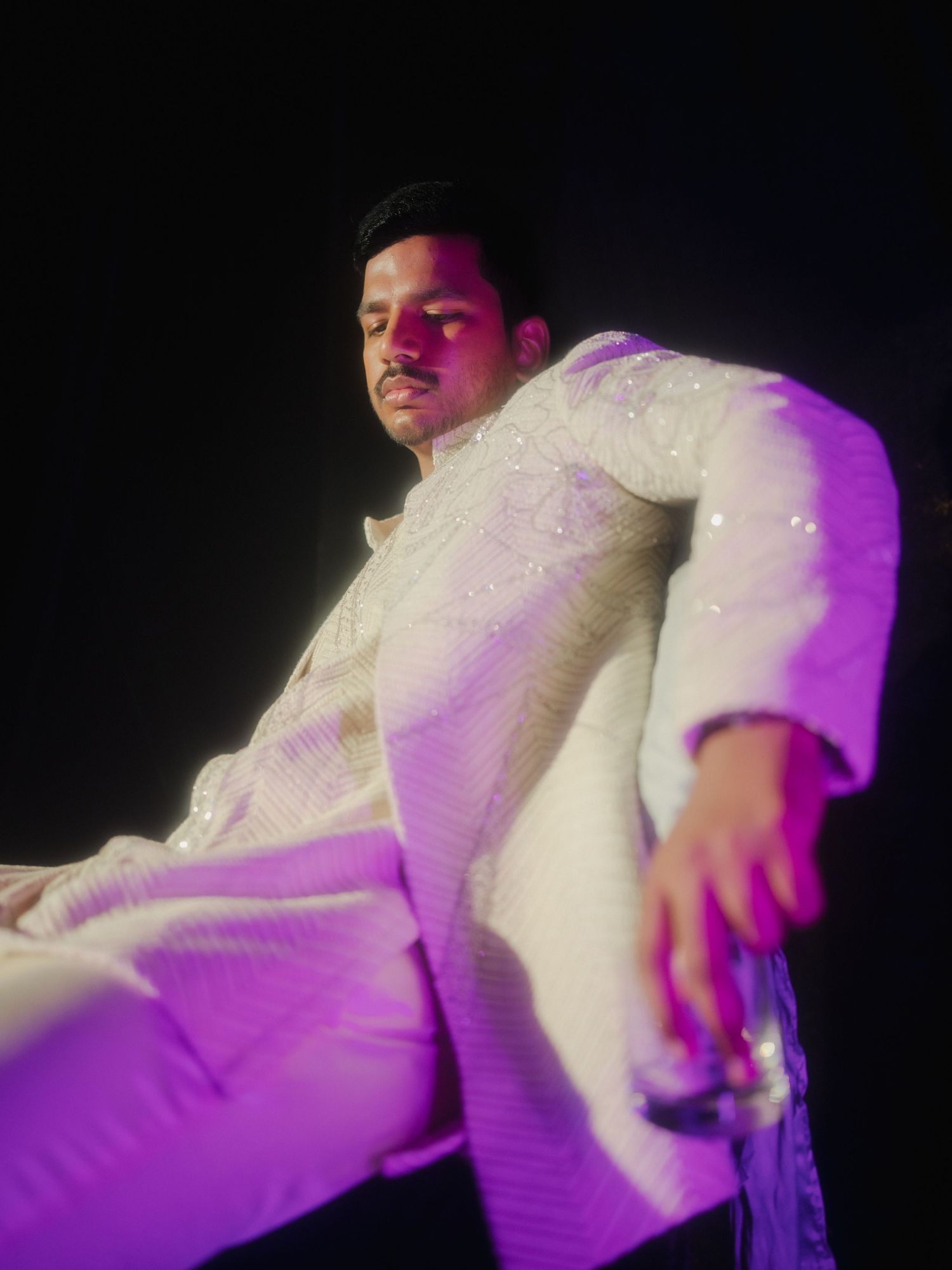Dancing figures in white formal attire illuminated by purple stage lighting during a celebration.