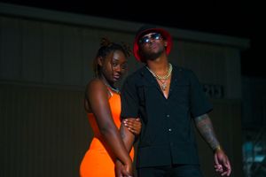 A couple in contrasting outfits shares an intimate moment in a dimly lit setting.