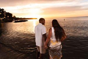 A couple walks along a beach shoreline during a beautiful golden sunset.