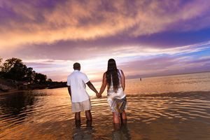 Silhouettes of two people standing together against a dramatic sunset over the ocean.