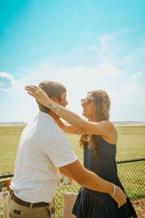 A couple shares a playful moment in a sunny outdoor setting with a white fence in the background.