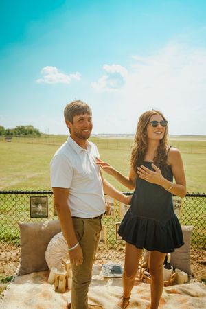A couple laughs together during a sunny outdoor photoshoot near a fence.