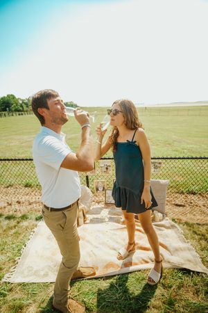 Two people share drinks and laughter during a sunny outdoor picnic.