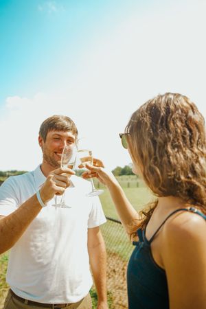 A couple toasts with champagne glasses in a bright outdoor setting.
