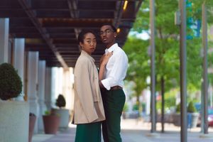 Couple embracing in an urban setting with modern architecture in the background.