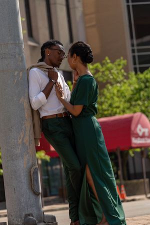 Two people sharing an intimate moment against a concrete pillar in an urban setting.