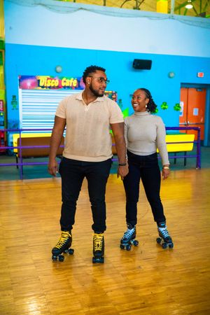 Two people roller skating together on a wooden floor in a colorful indoor rink.