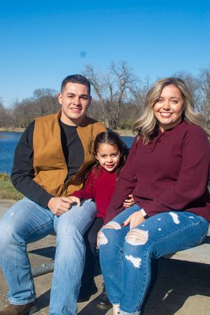 Family sitting and laughing together on a bench by a lake on a sunny day.