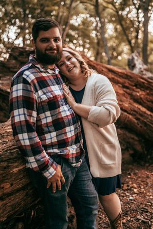 Couple sharing intimate laughs and embraces in a wooded autumn setting with fallen leaves.