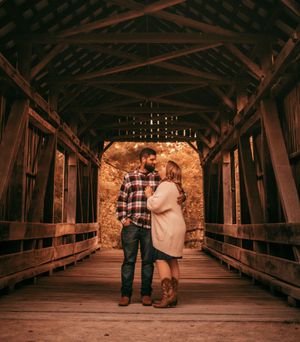 Romantic couple walking through a rustic covered wooden bridge at sunset.