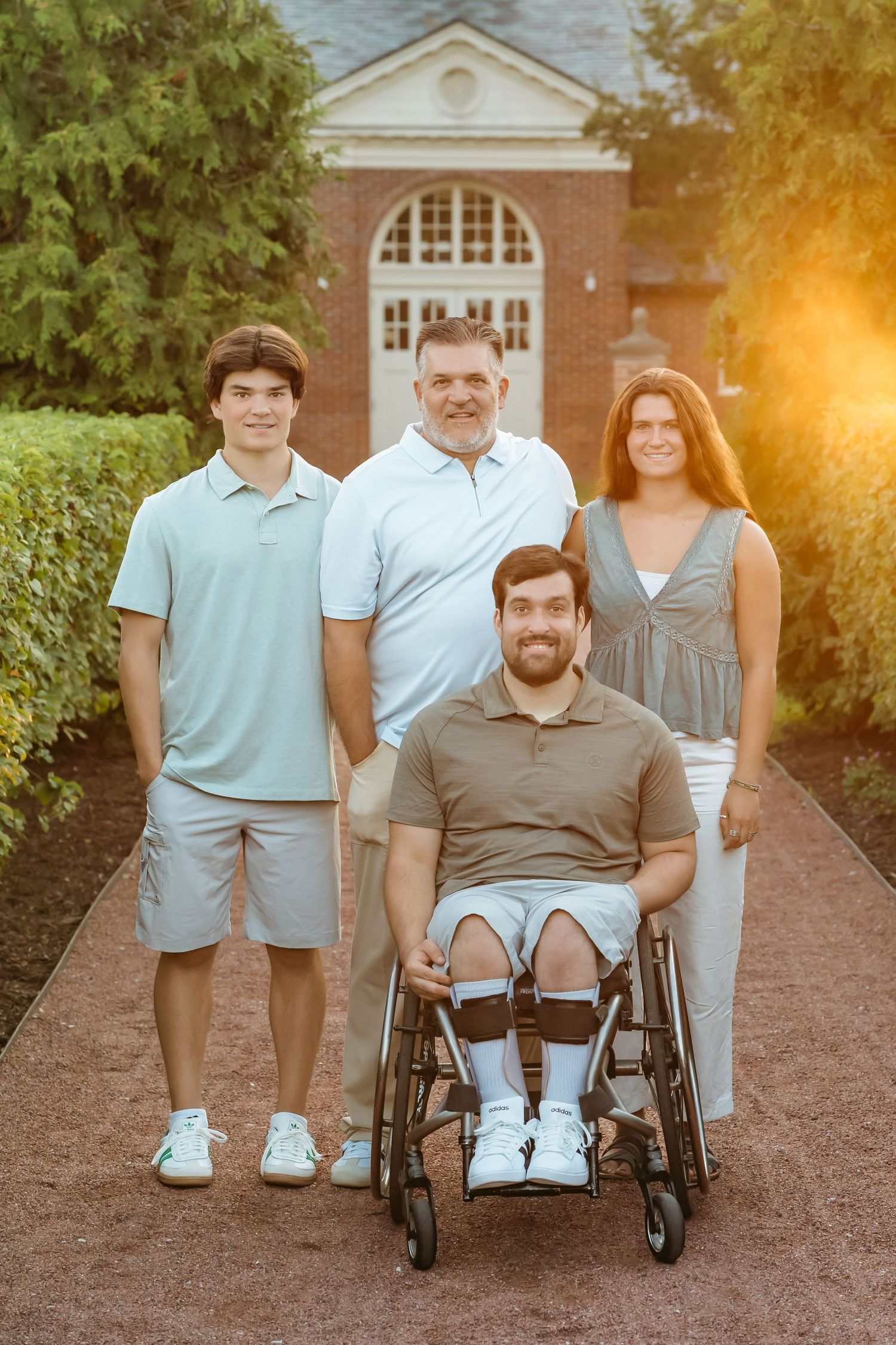 A group poses together outdoors on a brick pathway with warm sunset lighting in the background.