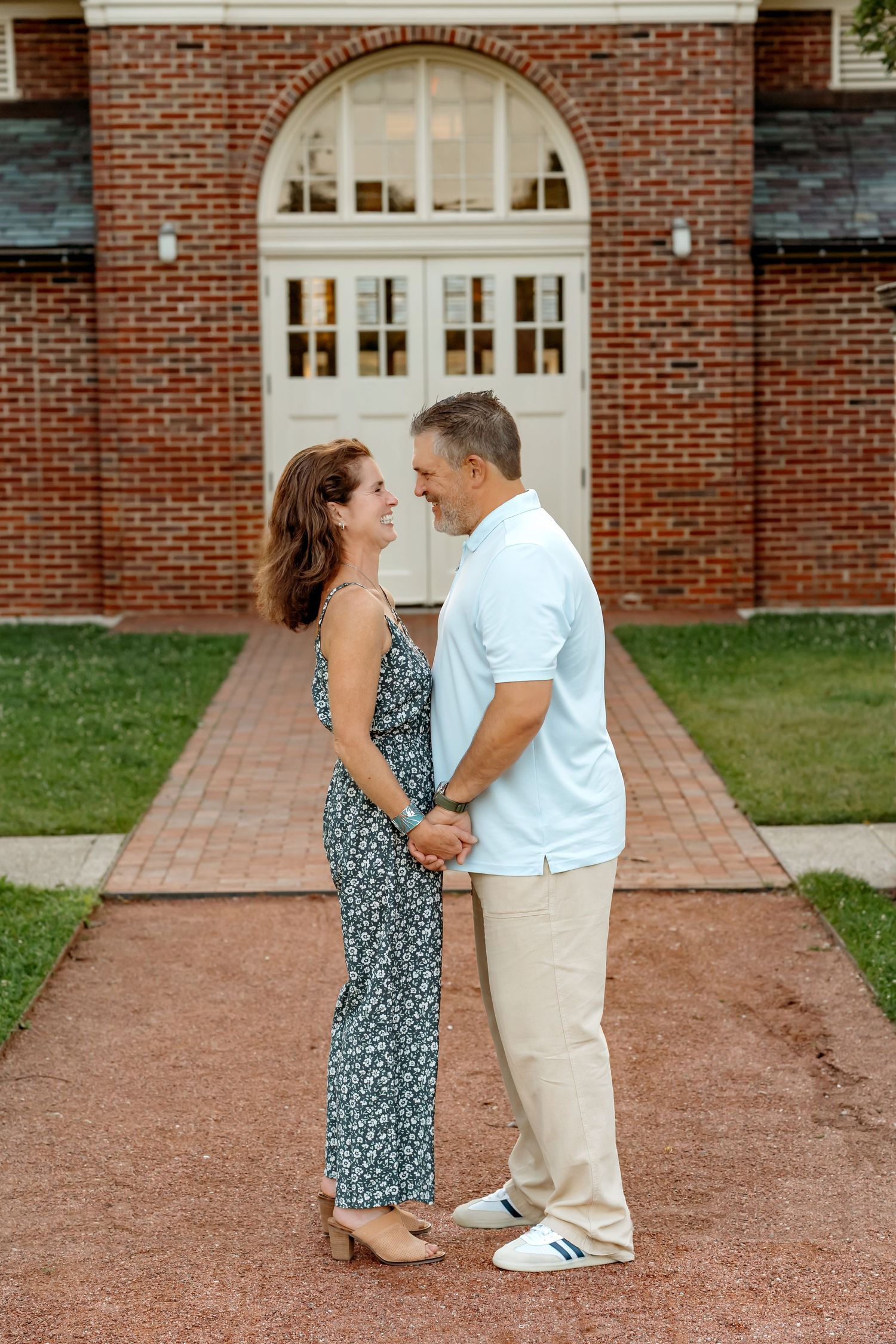 Romantic couple standing on brick path in front of arched doorway of historic building in summer.