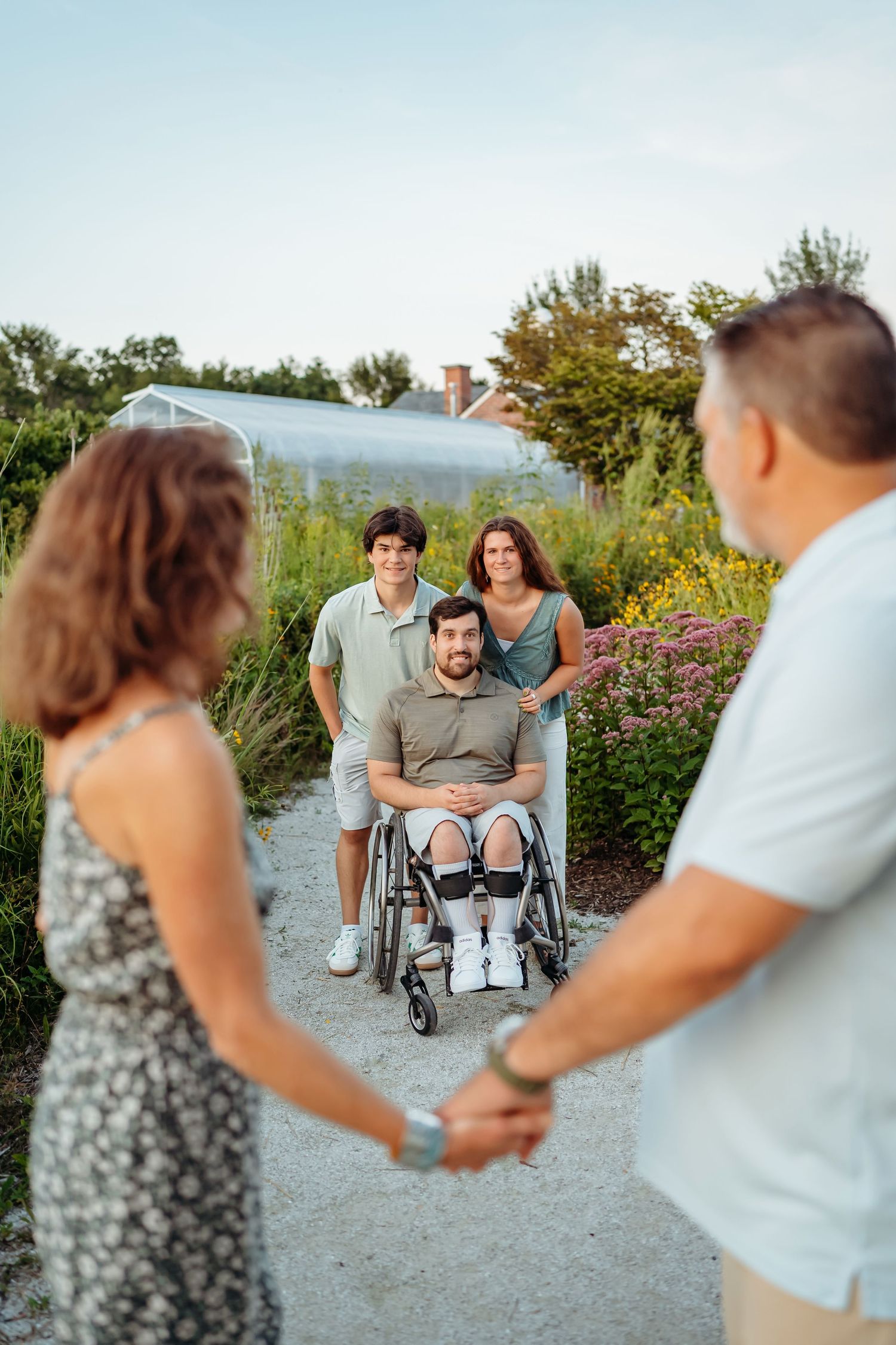 People gathered on a garden path with wheelchair, enjoying outdoor time together on a sunny day.