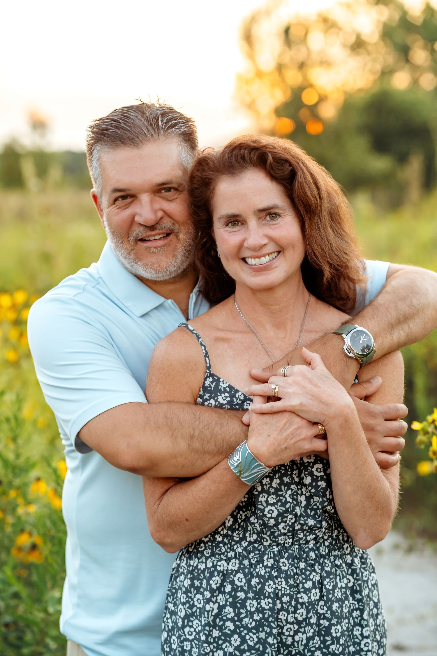 A couple embraces in a sunny meadow filled with yellow wildflowers during golden hour at sunset.
