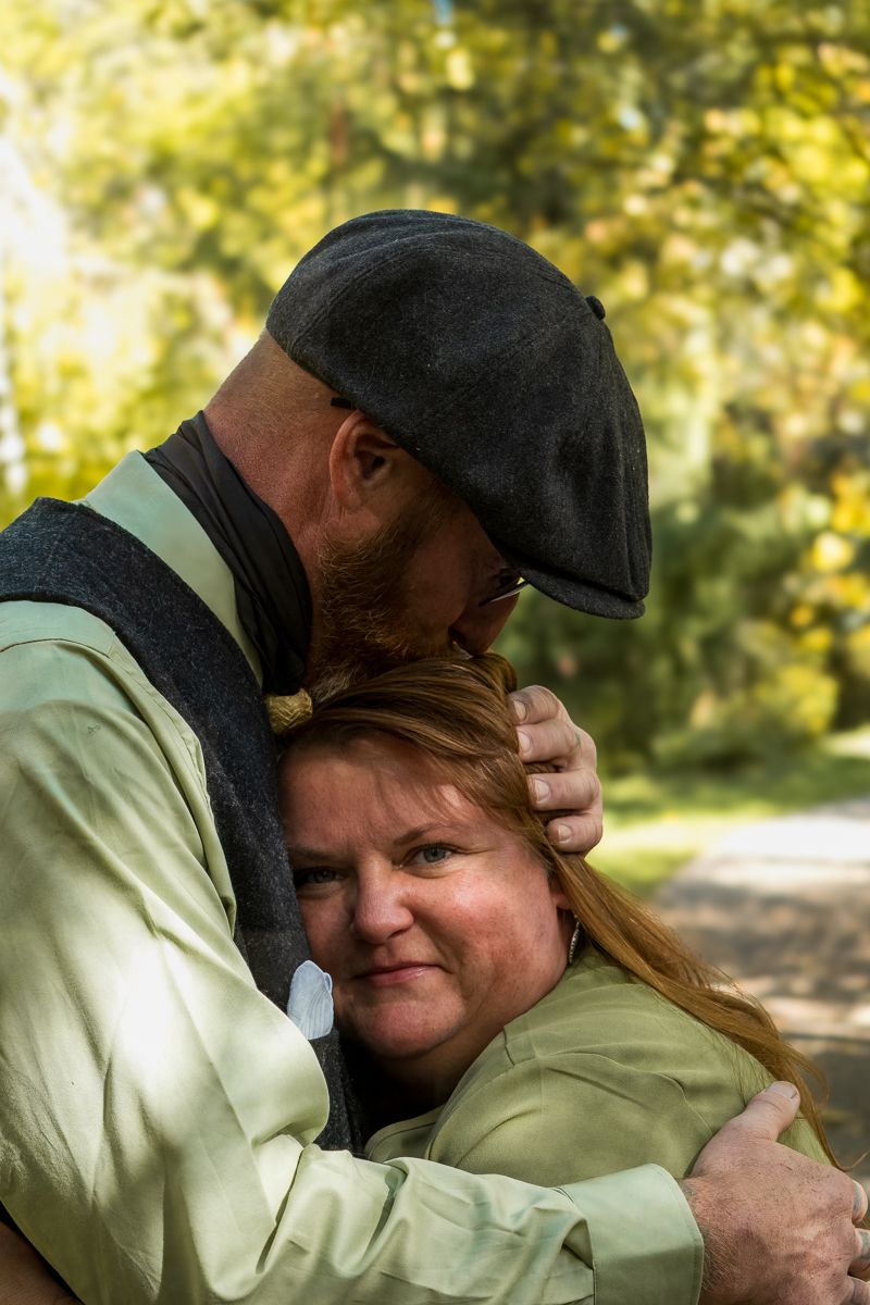 A couple shares a tender embrace outdoors on a sunny autumn day in a park setting.