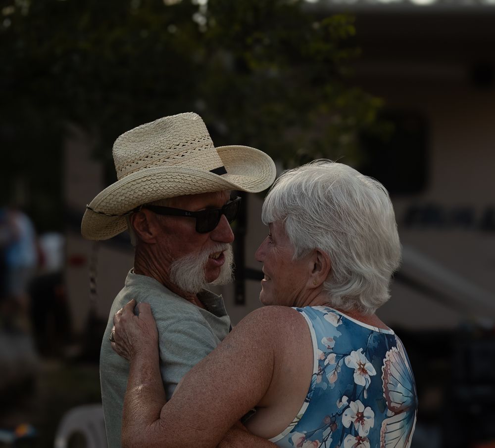 A couple in a cowboy hat and floral dress embrace and dance together at dusk.