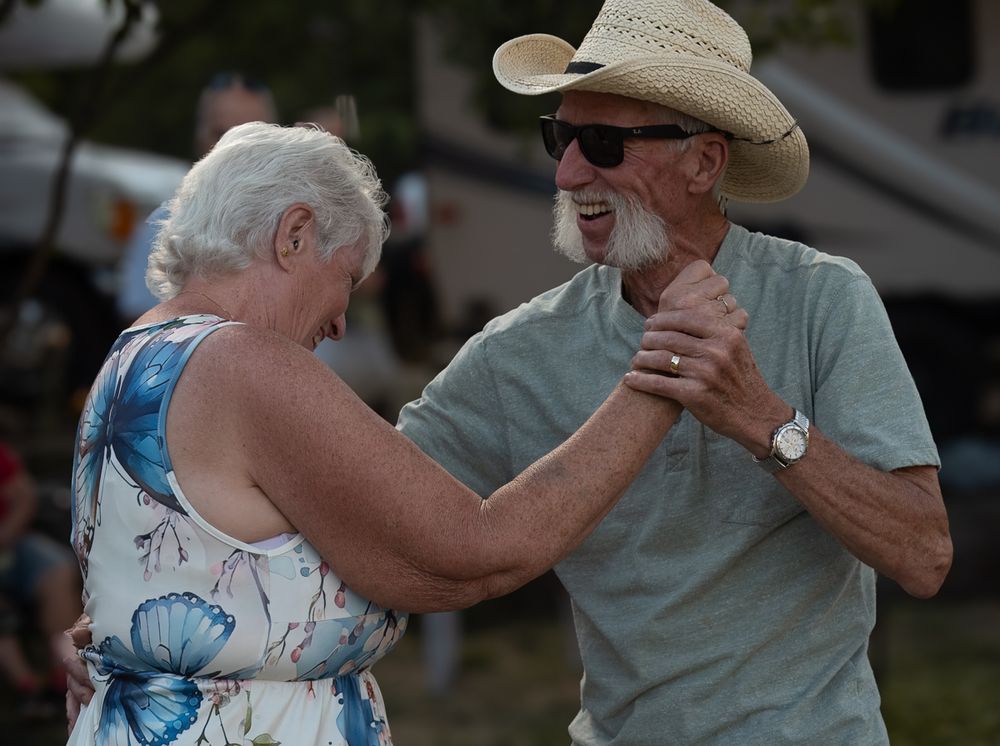 Two people share an intimate dance moment outdoors, the woman wearing a blue and white dress and man in casual attire.