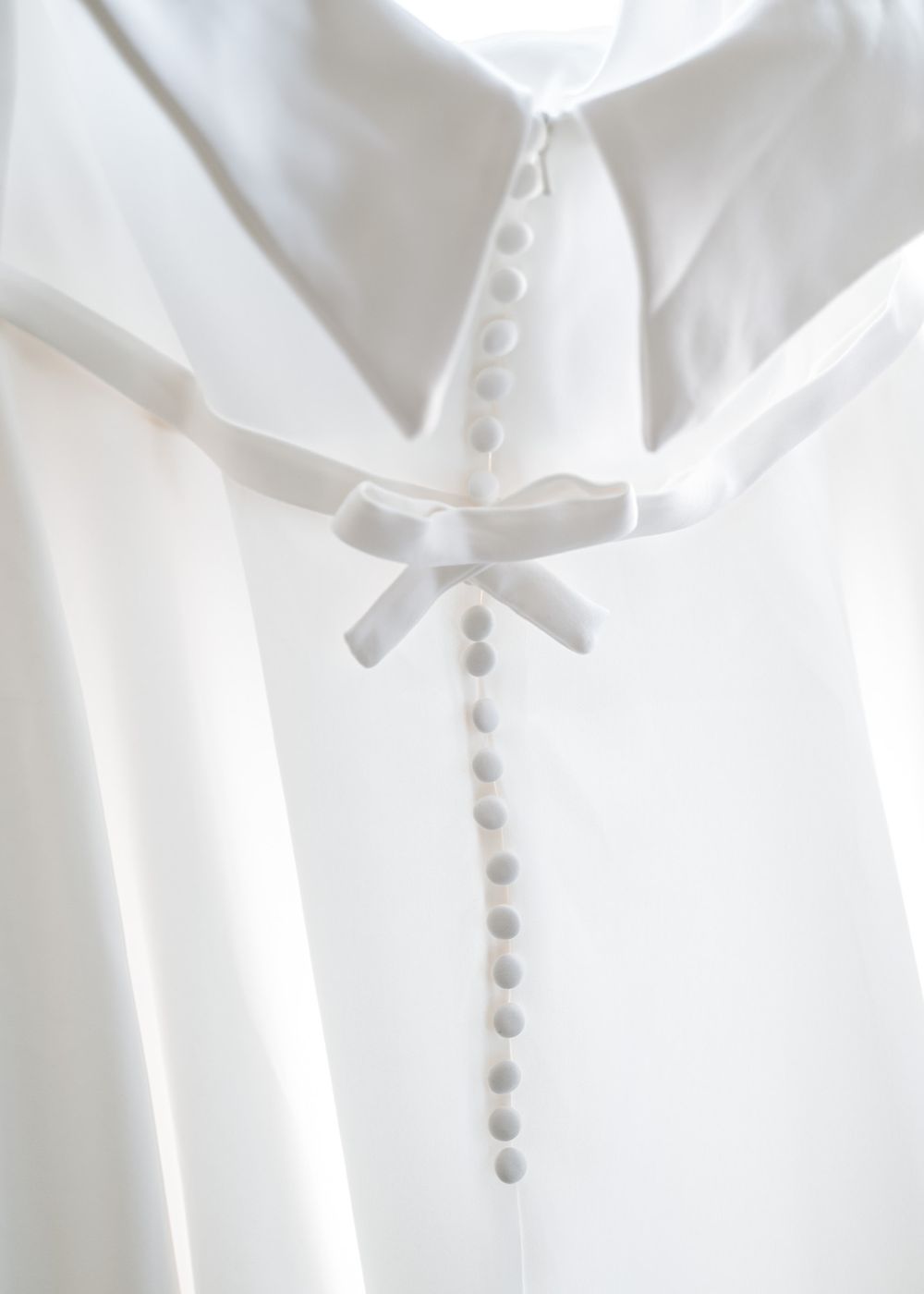 Close-up of a white wedding dress showing delicate button details and bow on the back.
