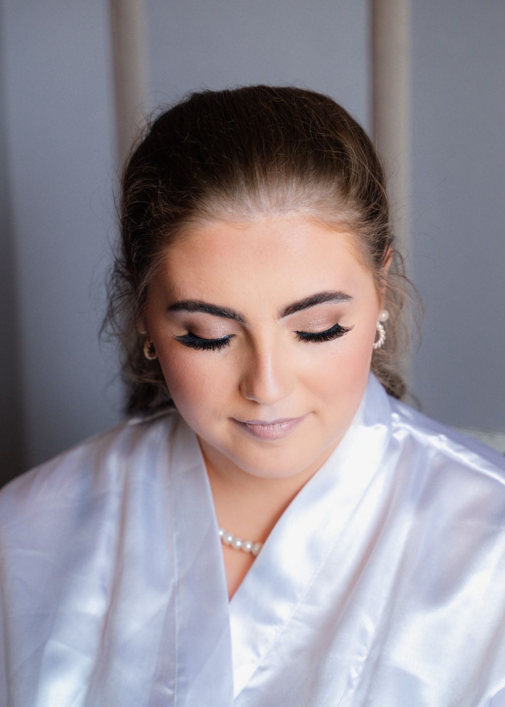 Beautiful bridal portrait showing soft makeup and pearl necklace against grey background.