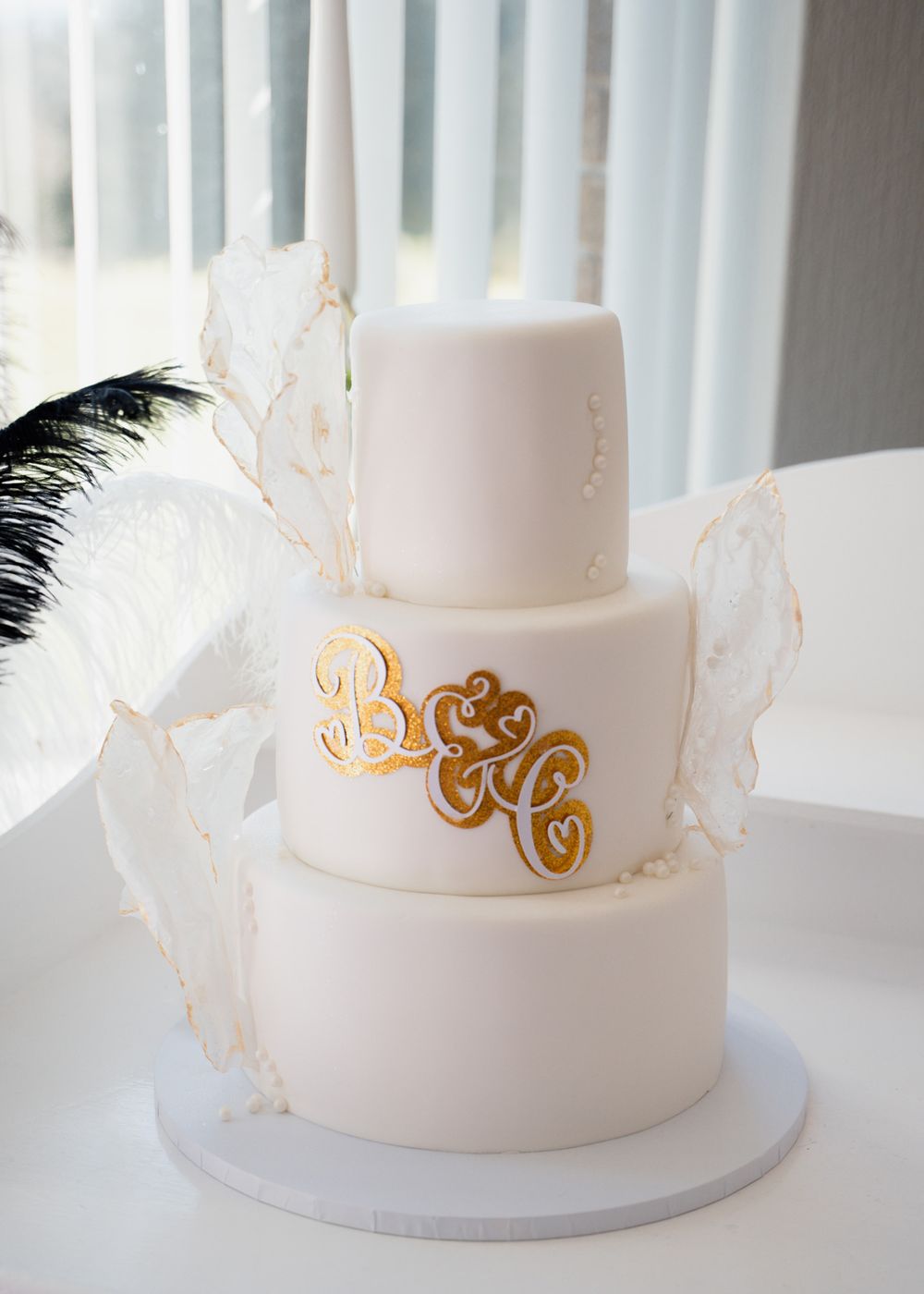 Elegant three-tier white wedding cake decorated with gold monogram and delicate branches.