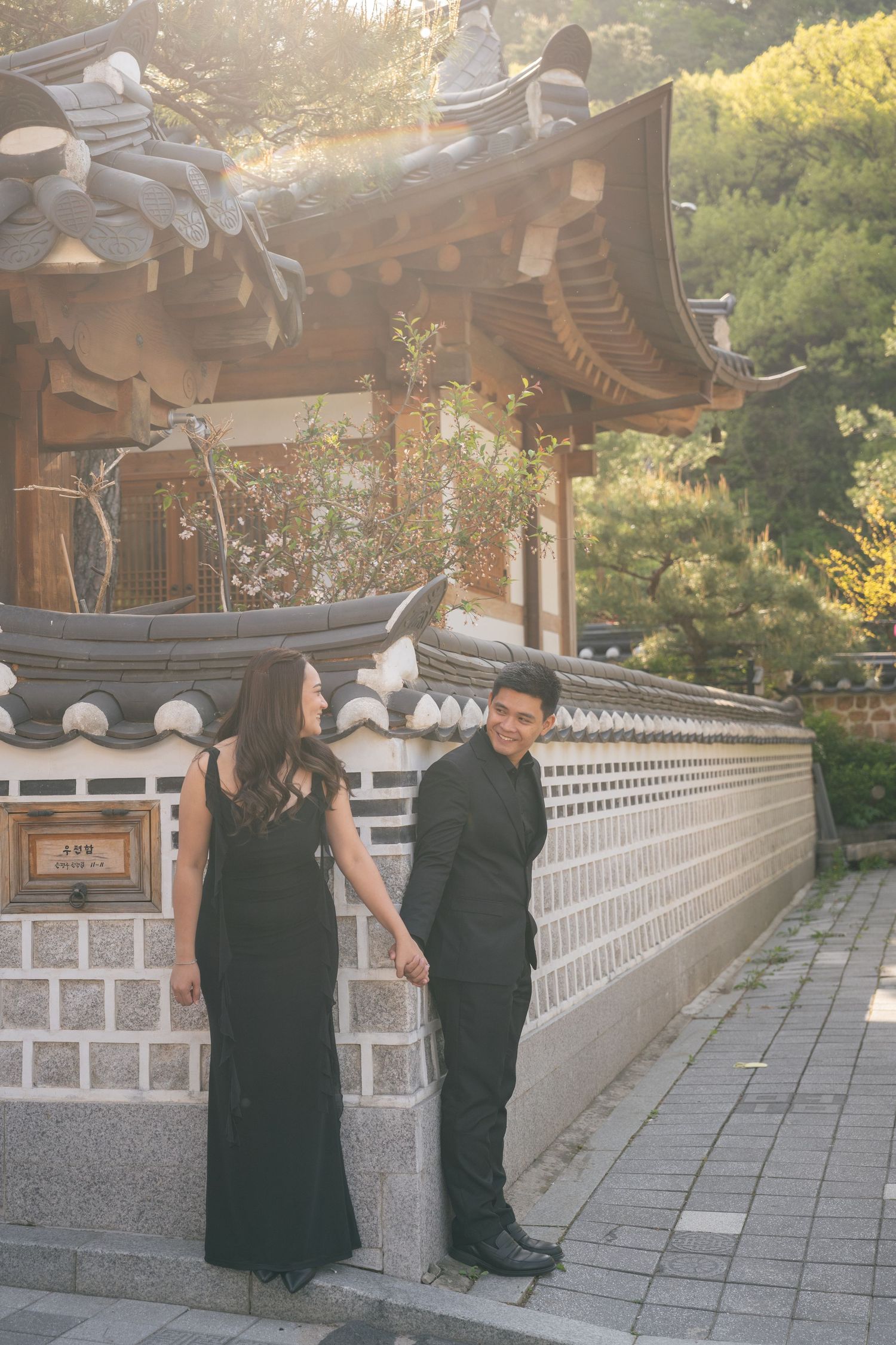 People in traditional Korean Buddhist monk attire walk along a temple corridor at sunset.