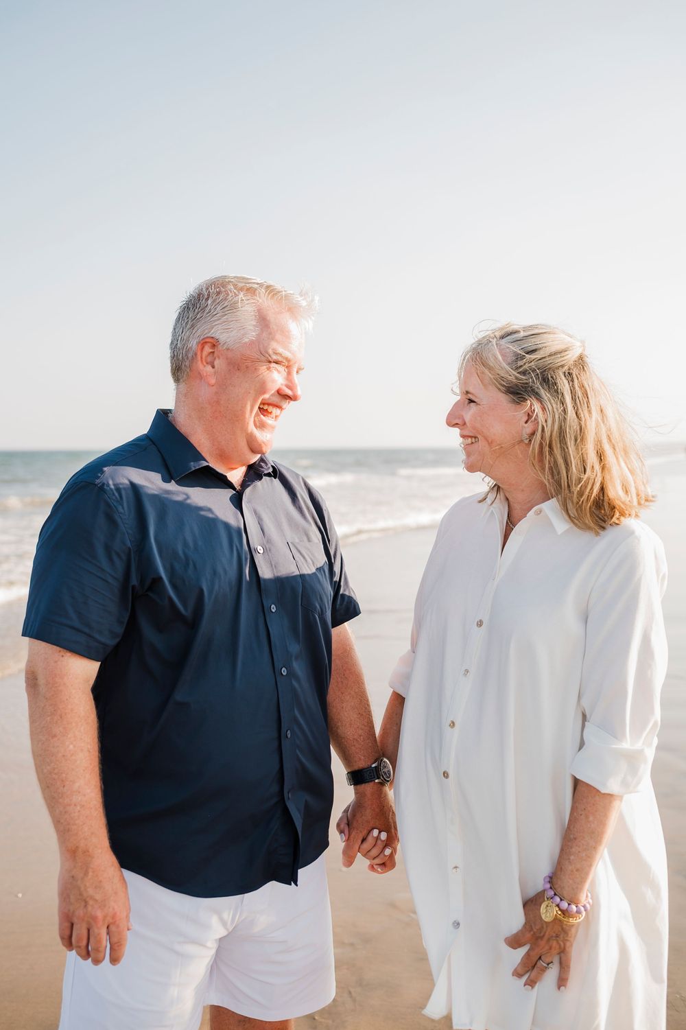 Couple in matching navy and white outfits sharing a joyful moment on the sandy beach.