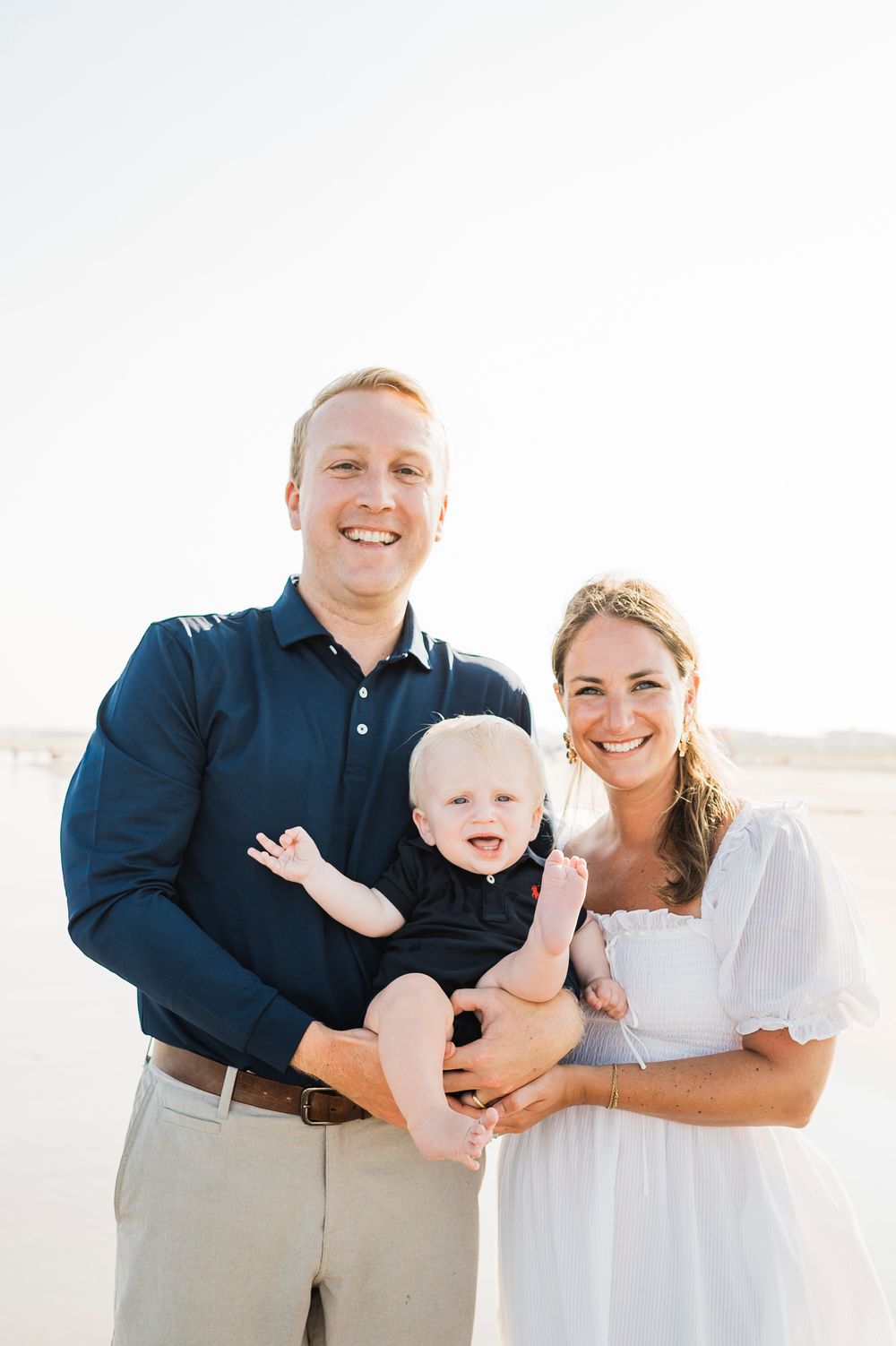 A family wearing coordinated navy and white outfits poses on the beach during a photoshoot.