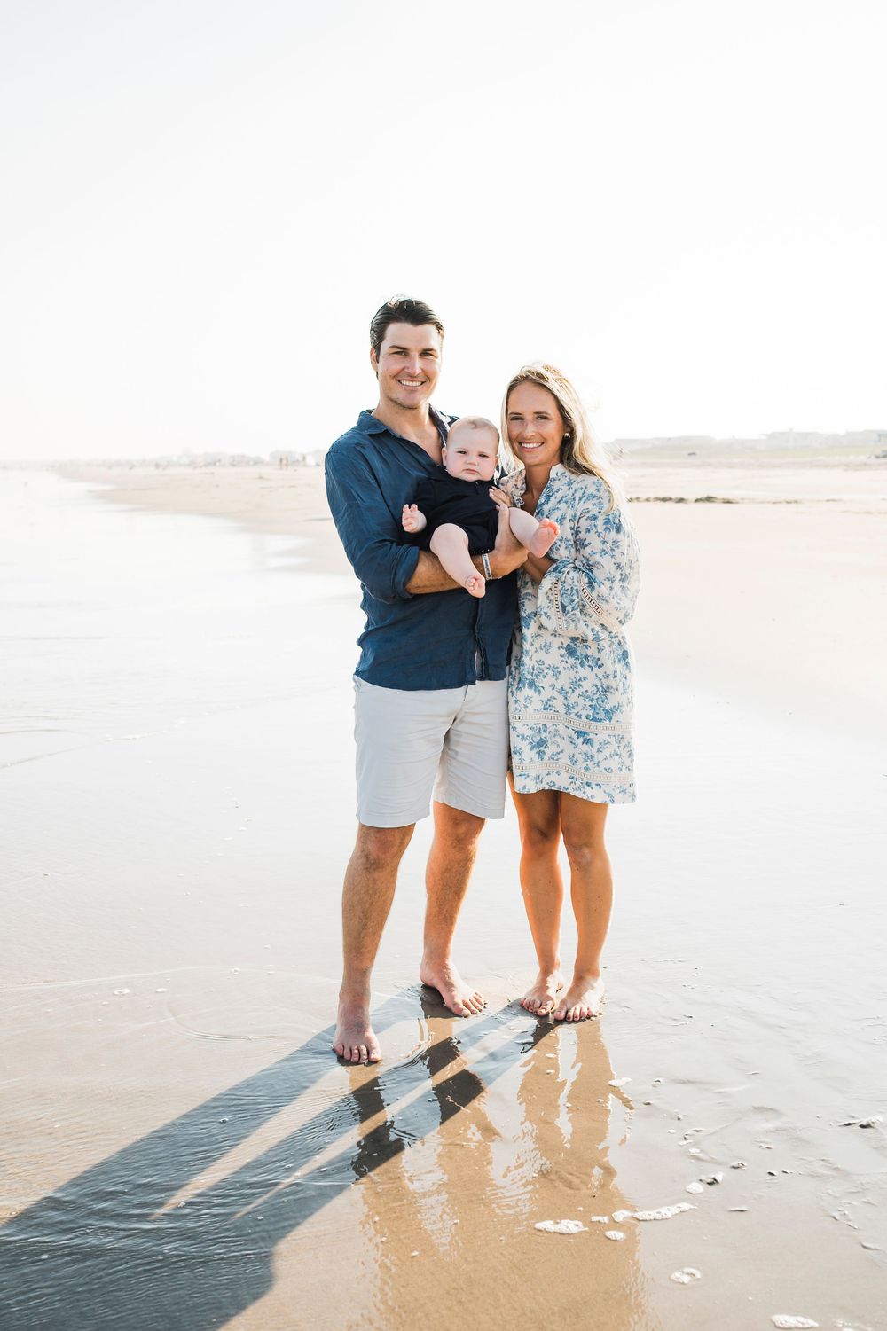 A family enjoys a tender moment together walking along a serene beach at sunset.