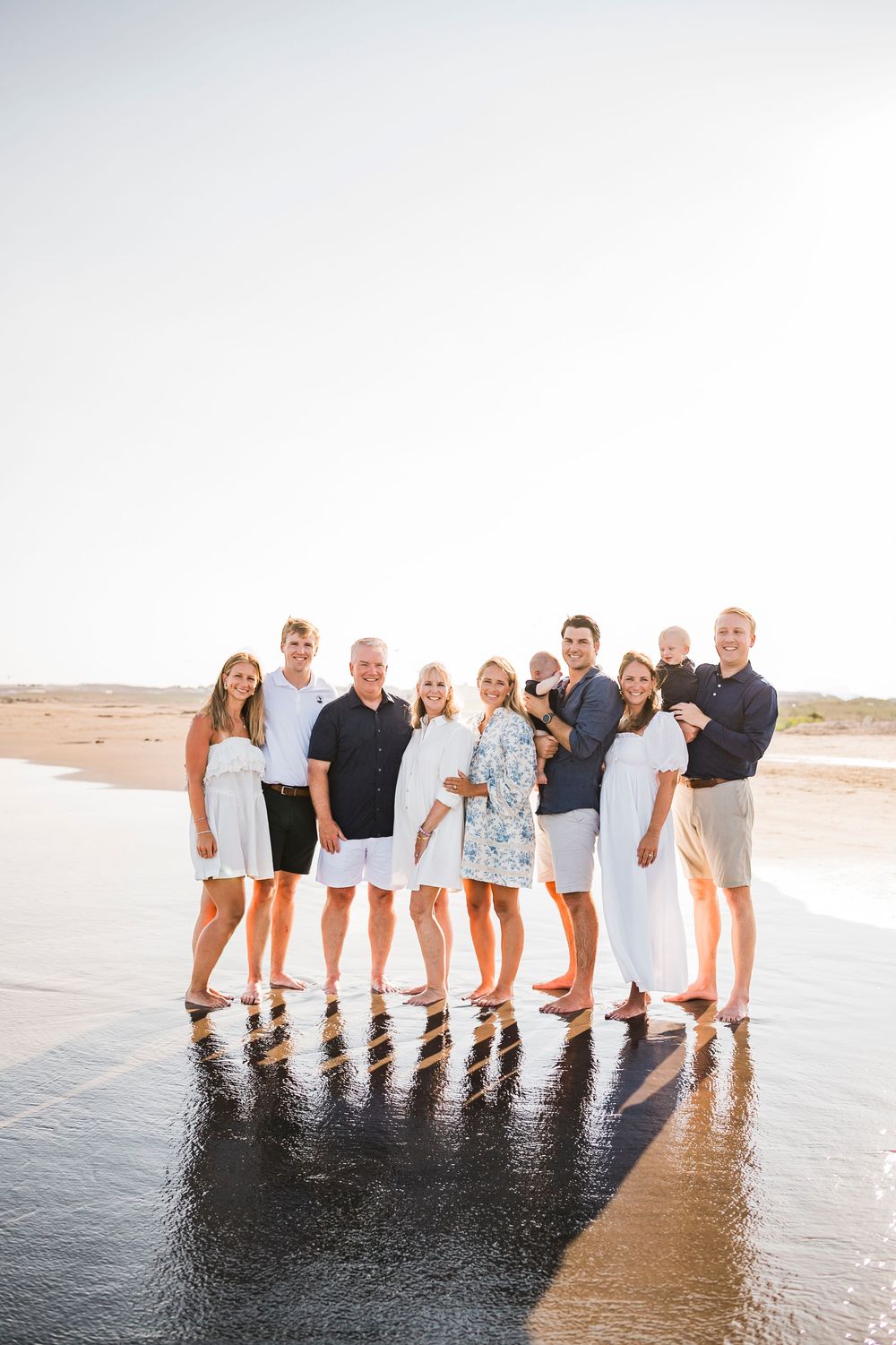Family members lined up along the beach shoreline at sunset creating long shadows on wet sand.